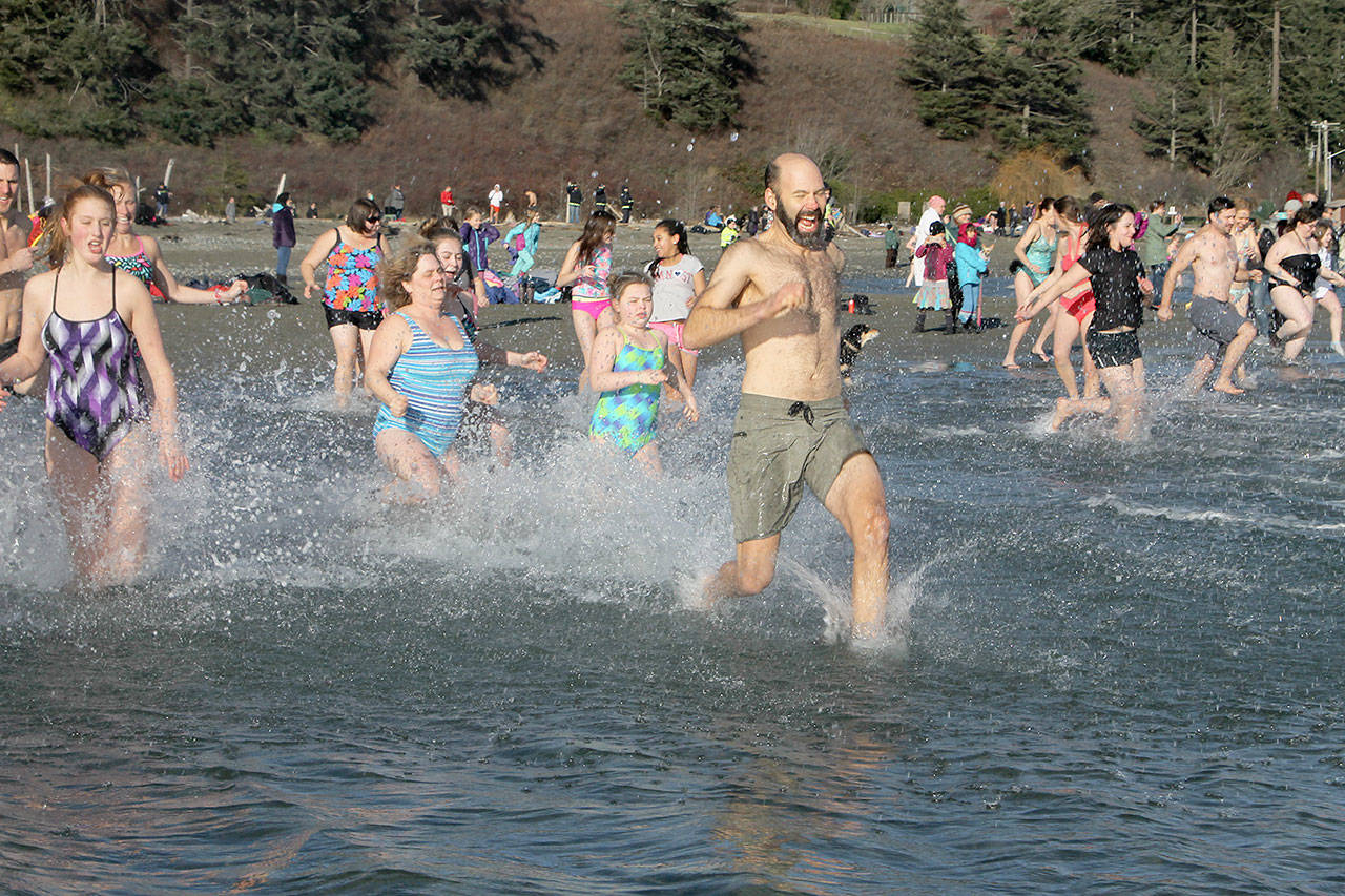 Doug Weigel leads the rush into the frigid waters during the 2017 Polar Bear Plunge at Double Bluff Beach Park. Around 150 people participated in the New Year’s swim. (Evan Thompson / The Record)