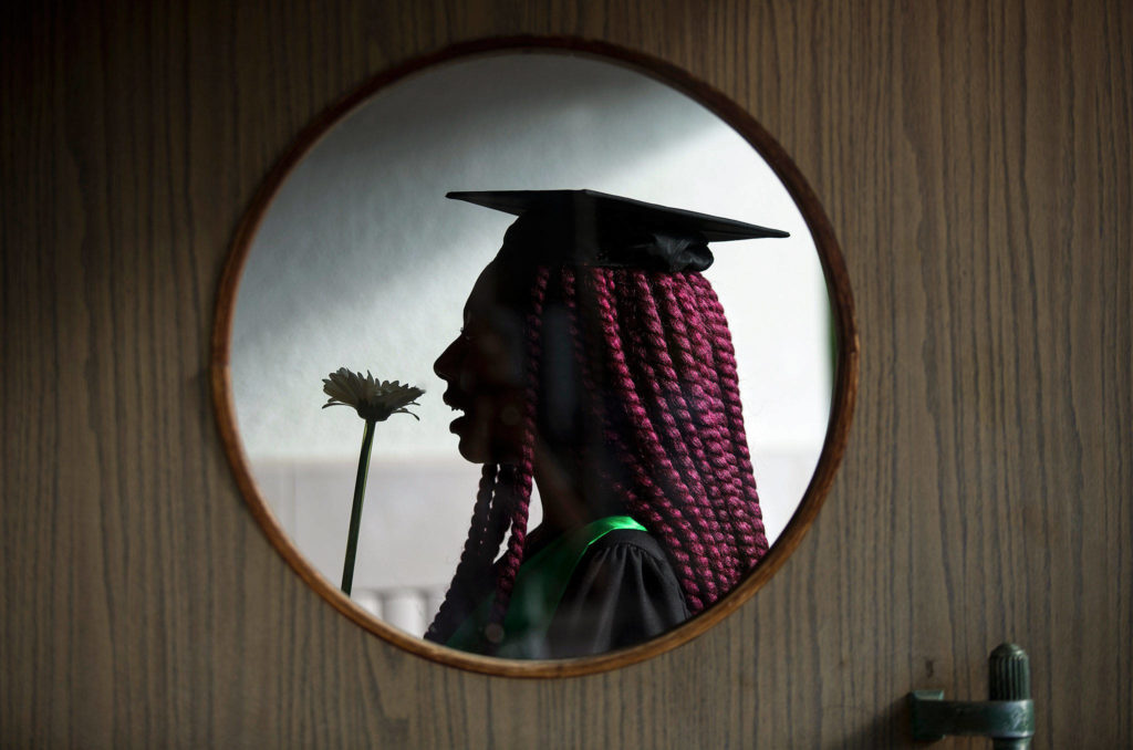 Seen through a door window, Marshawna Green smells a flower as she waits for the Sequoia High School graduation ceremony to begin at Everett Civic Auditorium on June 14 in Everett. (Andy Bronson / The Herald)
