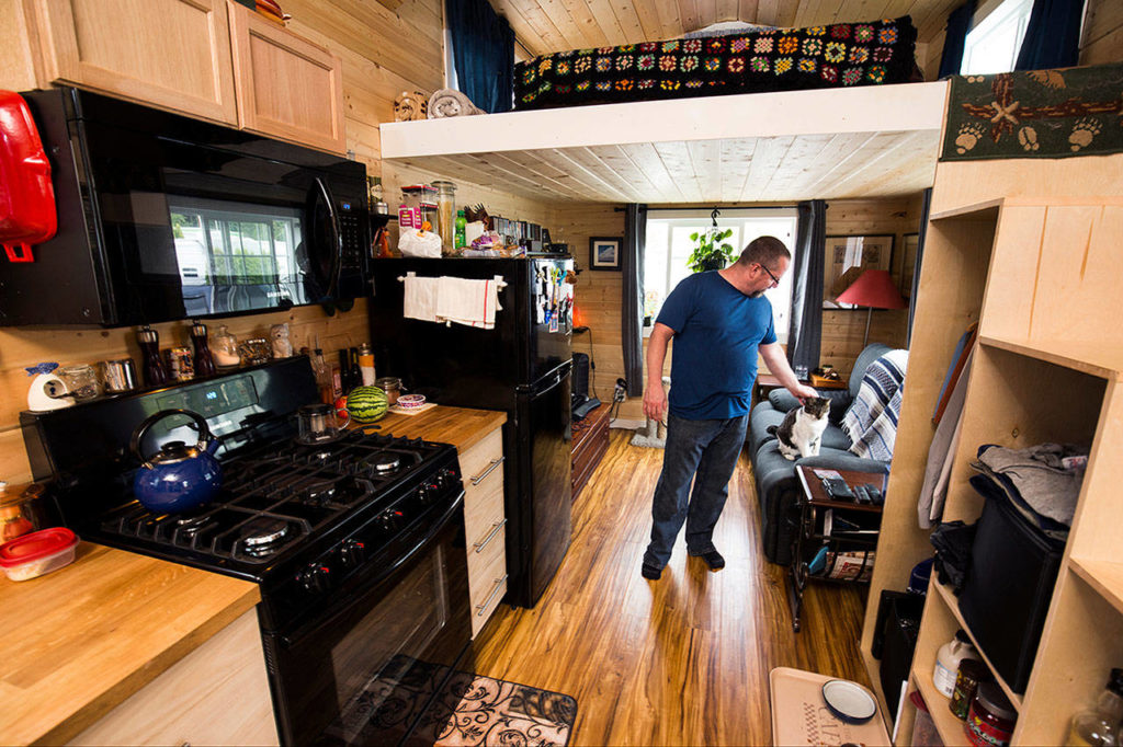 Michael Miller rubs the head of his cat, Underfoot, inside his tiny home at the Lakeside RV Park. The 245-square-foot house was built around his need for a full-sized kitchen. (Andy Bronson / The Herald)
