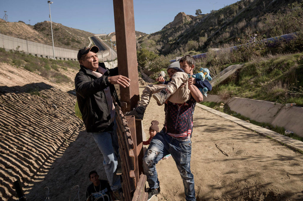 A man holds a Mexican migrant child Saturday, Dec. 29, as he jumps the border fence to get into the U.S. side to San Diego, Calif., from Tijuana, Mexico. Discouraged by the long wait to apply for asylum through official ports of entry, many migrants from recent caravans are choosing to cross the U.S. border wall and hand themselves in to border patrol agents. (AP Photo/Daniel Ochoa de Olza)

