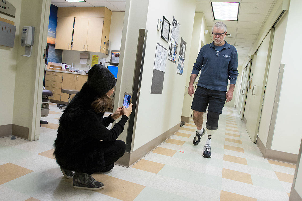 As John Sessions tries out a new leg sleeve in his prosthetic leg, his wife, Lucia, records video of his gait at the UW Medicine Prosthetics and Orthotics Clinic in Seattle. (Andy Bronson / The Herald)