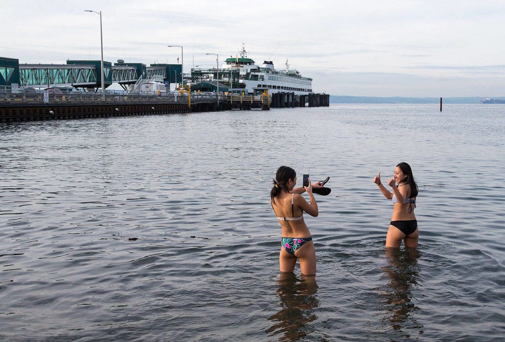After missing the first wave, Hope Juzon, left, and Catherine Do take photos as they hit the Puget Sound waters Tuesday, Jan. 1, during the annual Polar Bear Plunge at Brackett’s Landing in Edmonds. (Andy Bronson / The Herald)
