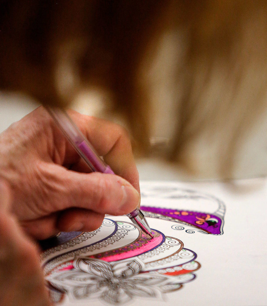 Paula Royset, 67, of Everett uses ink pens to color highly detailed drawings Wednesday evening at the Everett Public Library’s Coloring and Conversation program. (Dan Bates / The Herald)
