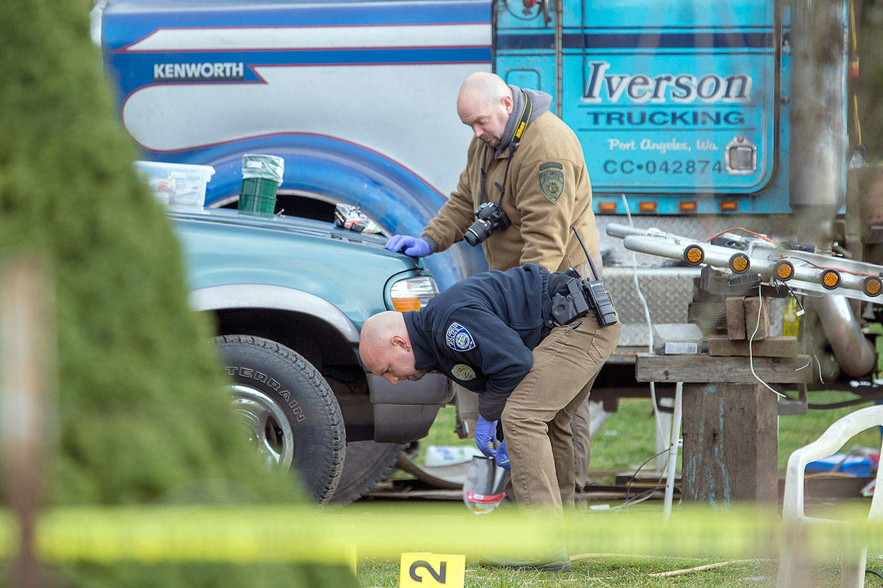 Port Angeles Police Department Detective Dave Arand and Officer Jeff Ordona look for evidence Wednesday at a home where three people were killed. (Jesse Major / Peninsula Daily News)