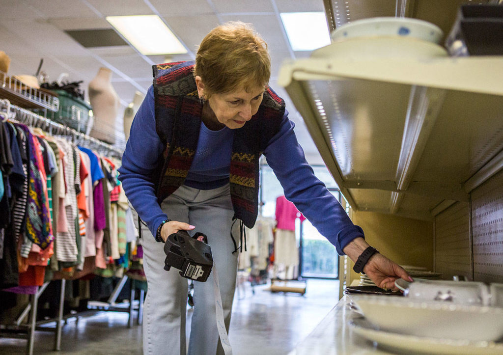 Karen Tiede prices plates and other kitchenware at the Edmonds Senior Center’s new thrift store. (Olivia Vanni / The Herald)
