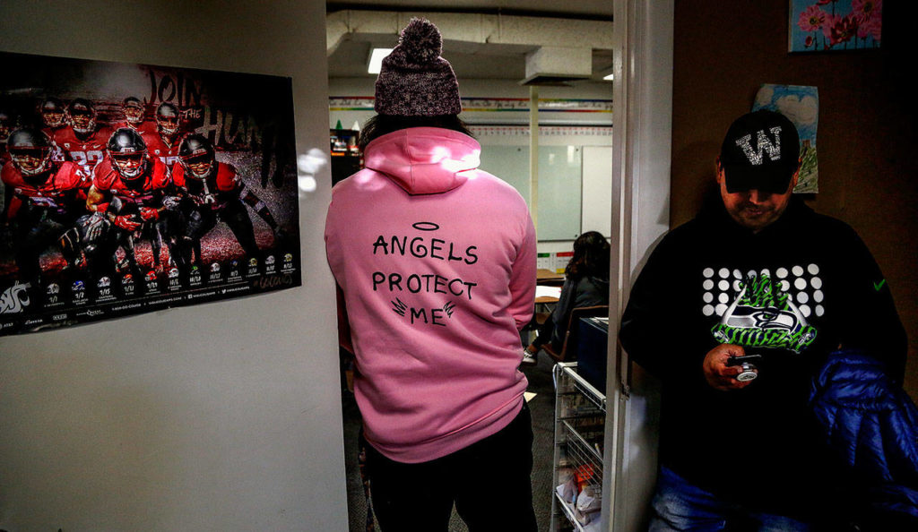 In the doorway of juvenile community corrections officer Calvin Nichols’ office, a 17-year-old boy watches activity in a classroom. Tulalip artist James Madison, who worked on the paddleboard project with the teens, checks his cellphone. (Dan Bates / The Herald)
