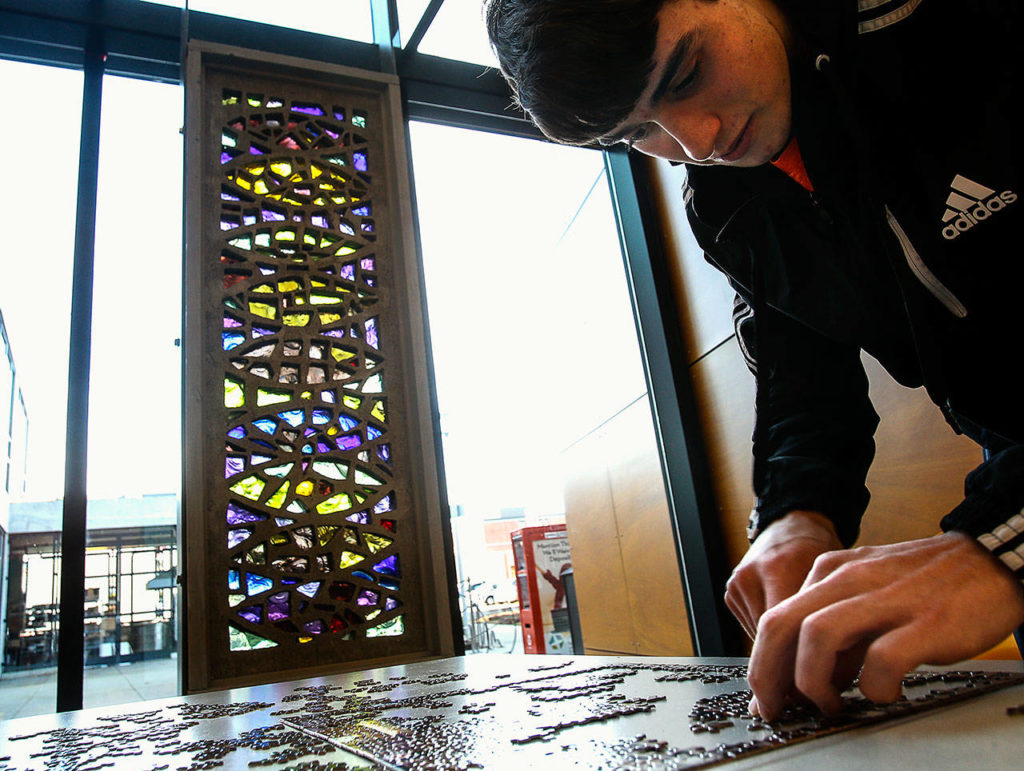 EvCC graphics design student Nathan McGinty works on a jigsaw puzzle near Russell Day’s untitled concrete and Blenko glass sculpture by a window in Whitehorse Hall. Day, a longtime art instructor at the college, died Monday. (Dan Bates / The Herald)
