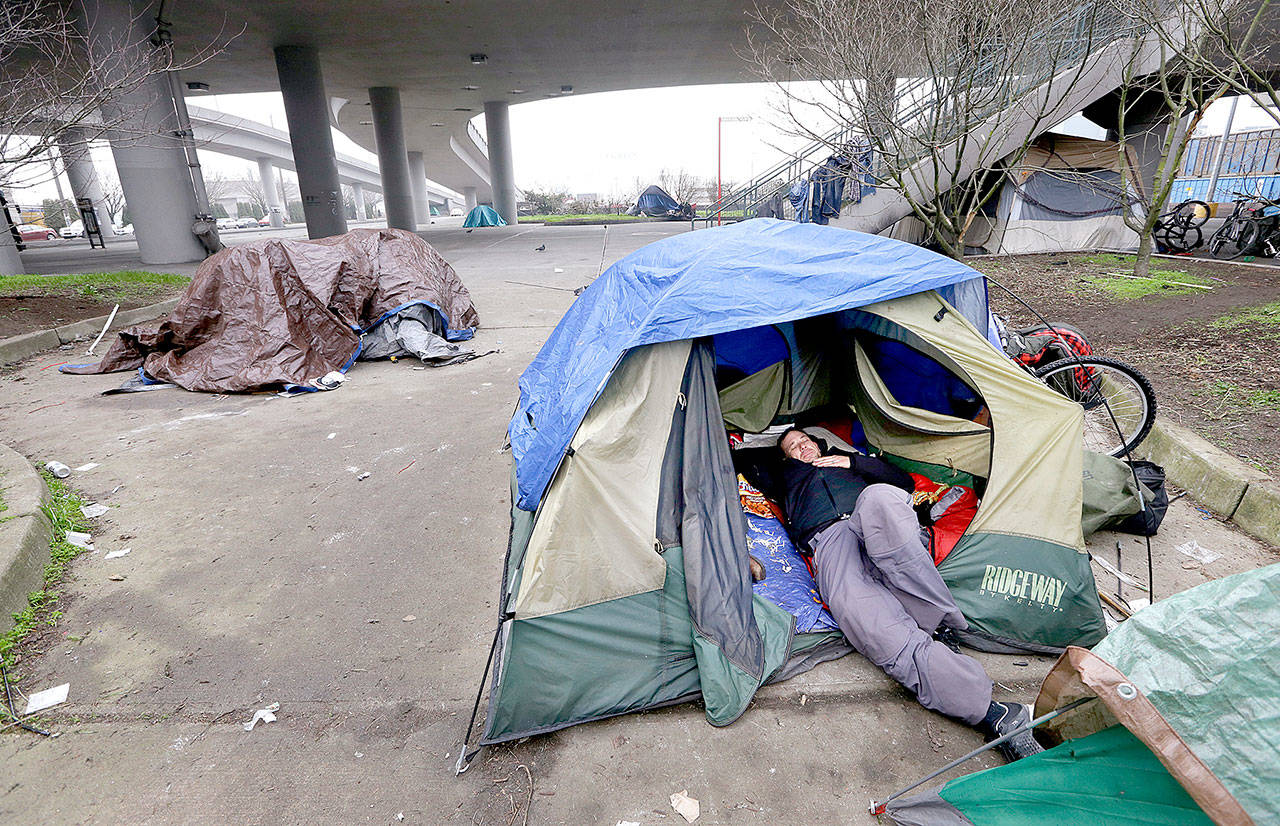 A man lies in a tent and others are camped nearby under and near an overpass in Seattle. (AP Photo/Elaine Thompson, File)