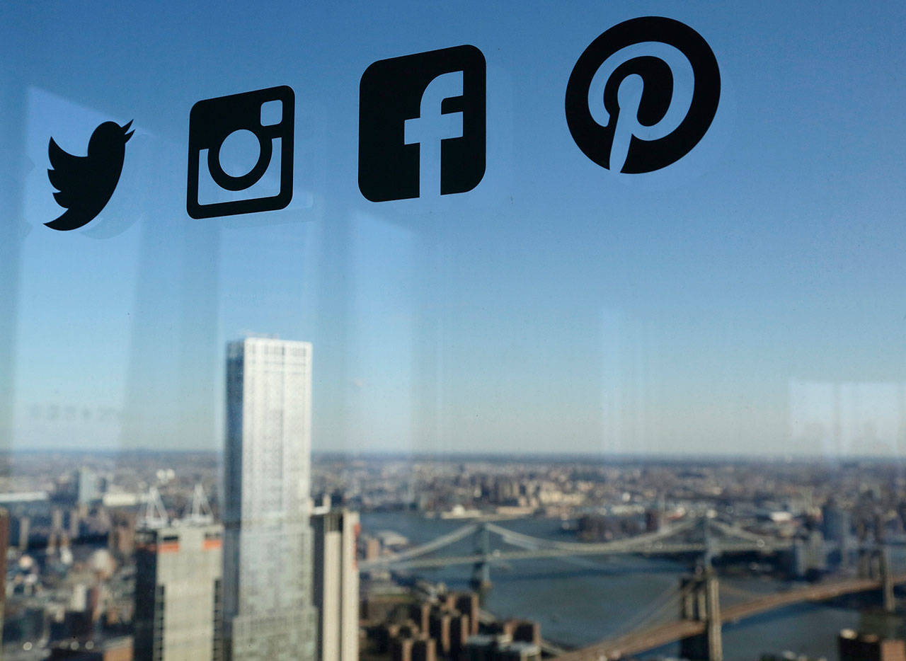 Icons for Twitter, Instagram, Facebook and Pinterest are displayed on a window in New York in 2016. Nearly half of U.S. households carry credit card debt, which means many of the friends making you jealous on Instagram may not be able to afford the vacations they post about. (Mark Lennihan / Associated Press)