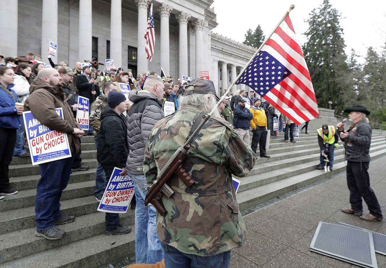 Dave Brown of Tumwater displays an upside-down U.S. flag in the barrel of his gun as he takes part in a gun-rights rally Friday at the Capitol in Olympia. (AP Photo/Ted S. Warren)