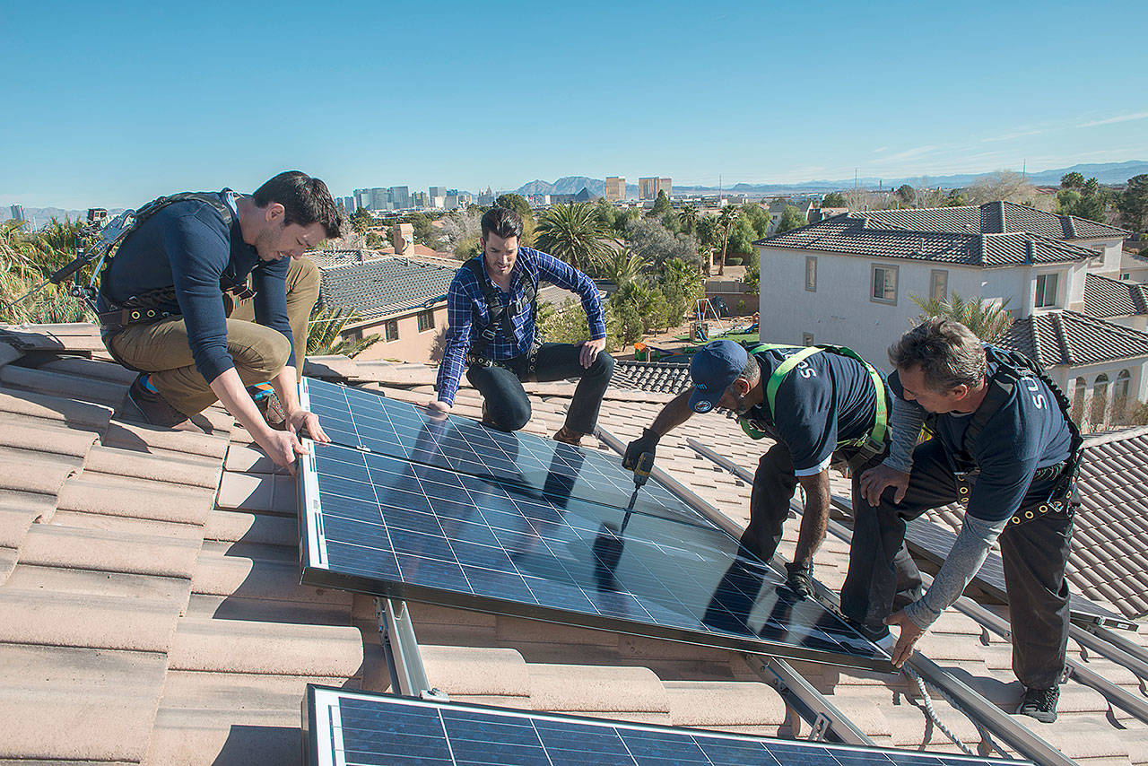 Twin brothers Drew Scott, left, and Jonathan Scott, center, stars of the HGTV show “The Property Brothers” and solar enthusiasts, help install Sunrun solar panels on a newly renovated “smart home” in Las Vegas in 2015. (John Harrington/ Sunrun)