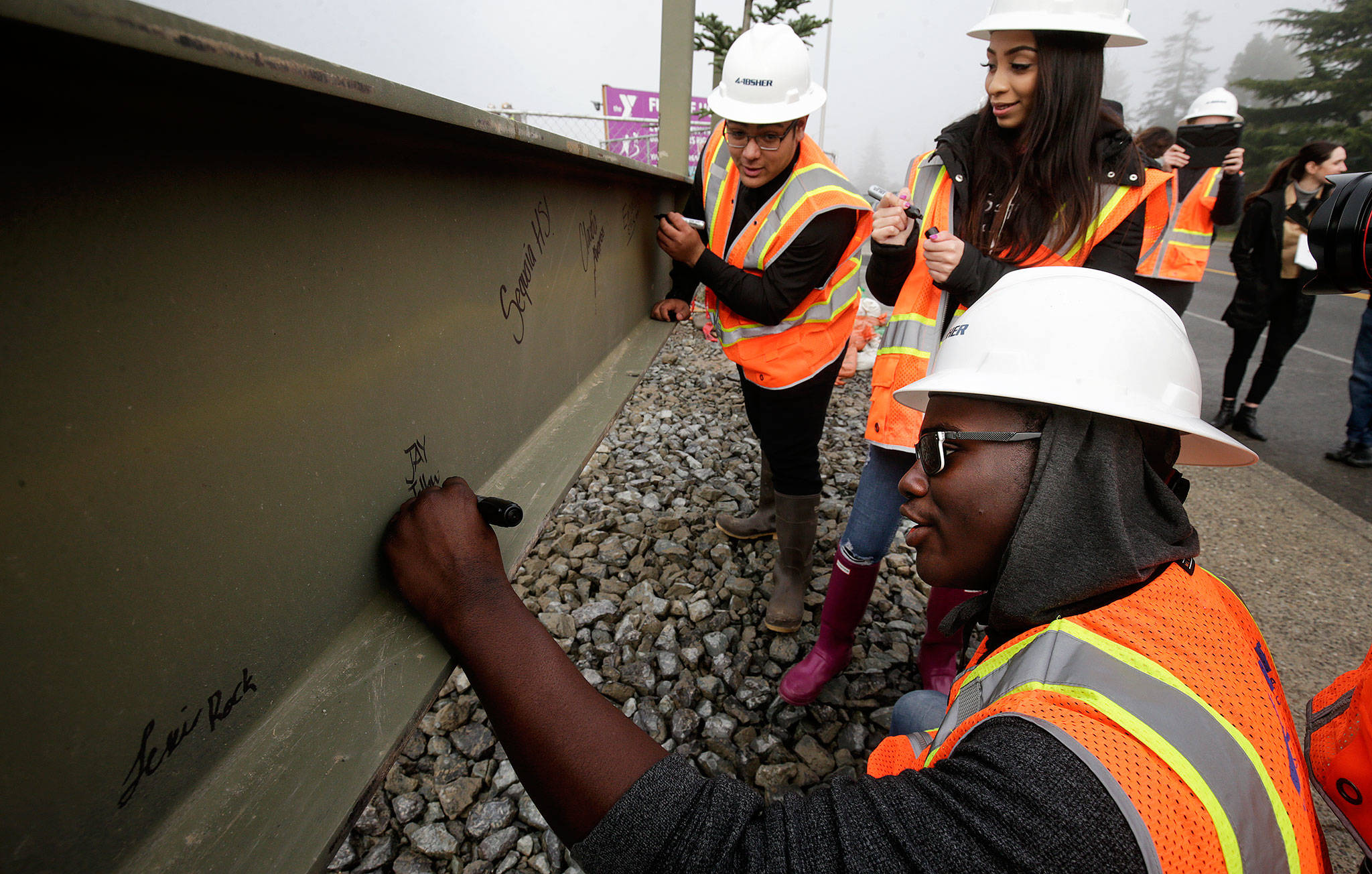 Sequoia High students Sarjo Jallow (lower right), Emanuel Ellis (top left) and Claudia Infante sign their names on the final beam for the roof of the new YMCA building on Colby Avenue on Friday in Everett. (Andy Bronson / The Herald)