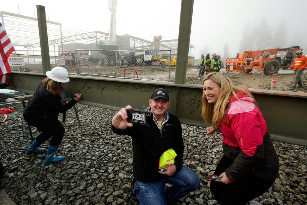 Michael and Heather Wallace take selfies after signing their names on the final beam for the roof of the new YMCA building on Colby Avenue in Everett on Friday. (Andy Bronson / The Herald) 
