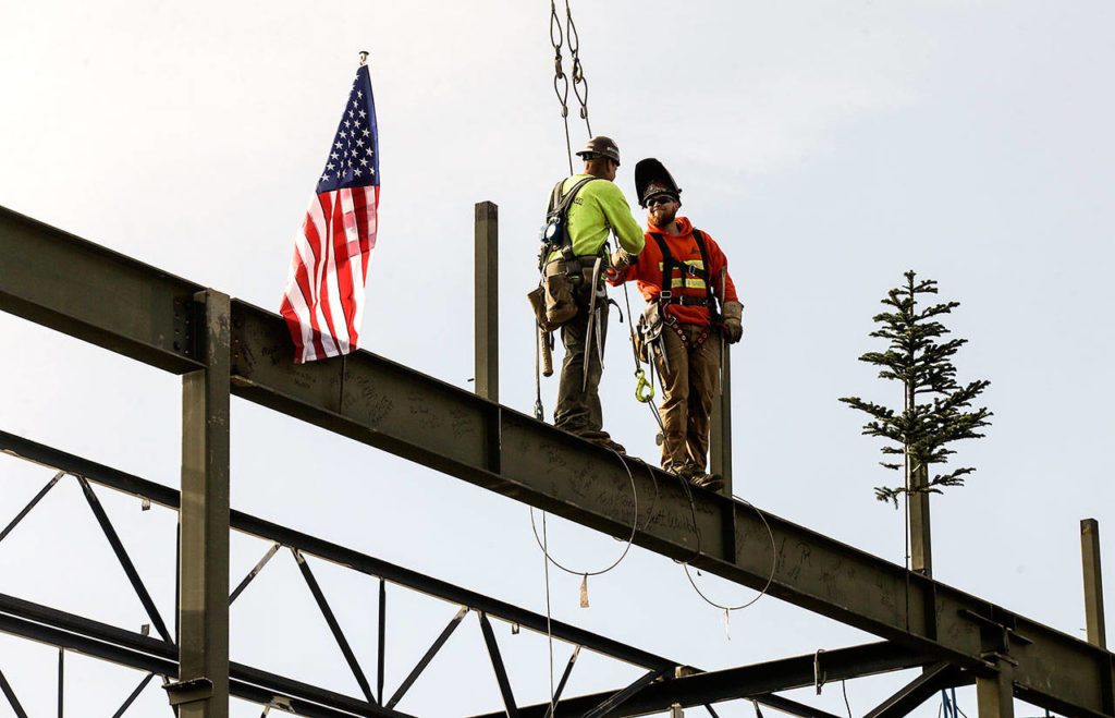 After putting the beam in place, two workers shake hands as part of the “topping off’ ceremony for the final beam on the roof of the new YMCA building on Friday in Everett. (Andy Bronson / The Herald)
