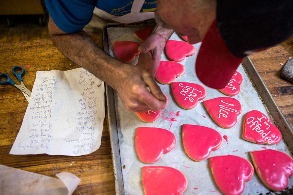 Ken Bellingham frosts his red heart cookies with sayings from his phrase sheet in addition to some that he comes up with on the spot at Edmonds Bakery. (Olivia Vanni / The Herald)
