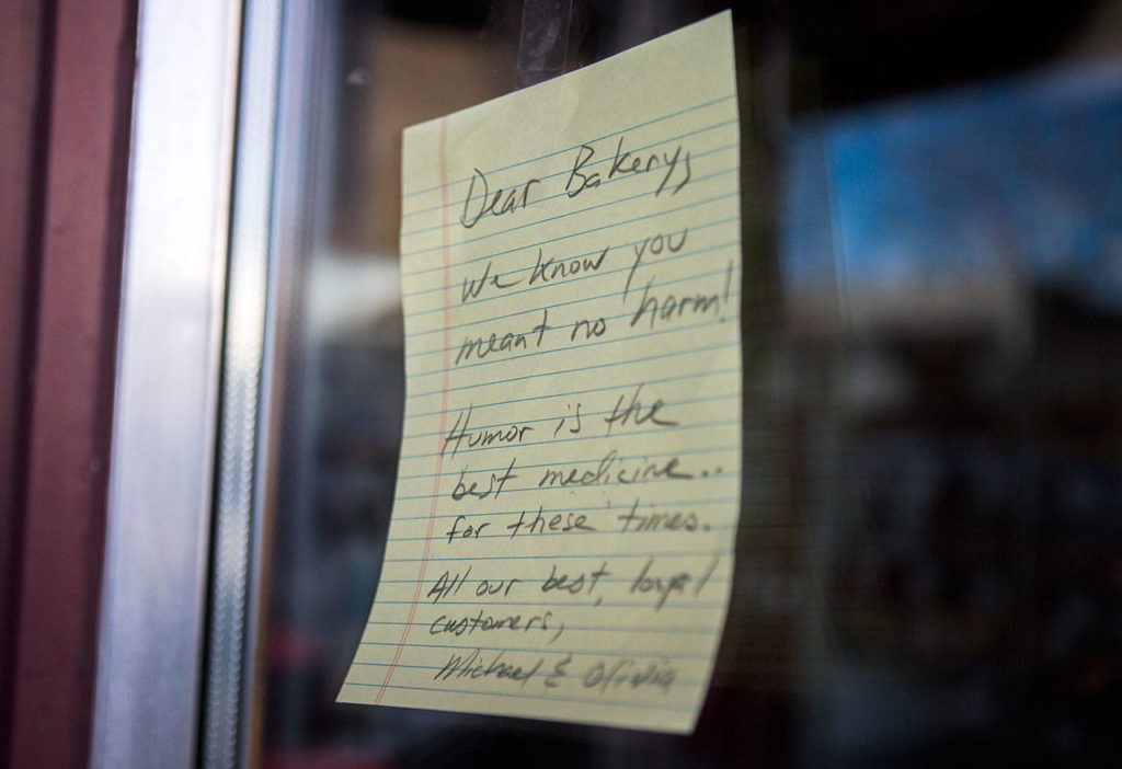 A note from a customer hangs next to the entrance of the Edmonds Bakery expressing support of the contentious cookie. Someone else put up a “Stop the Hate” sign a few inches away. (Olivia Vanni / The Herald)
