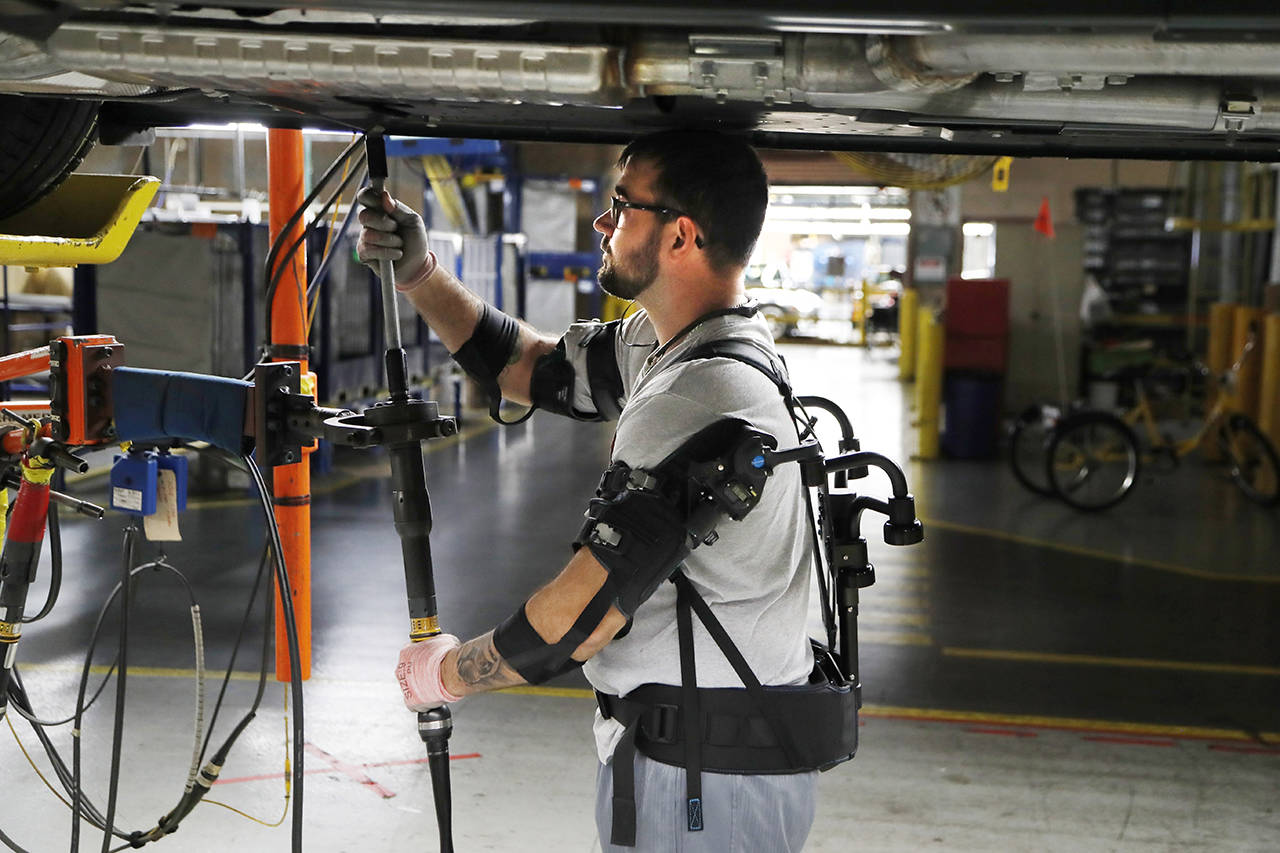 In this 2018 photo, Ford assembly line worker Nicholas Gotts, wearing a new wearable technology called an EksoVest, works on a vehicle in Flat Rock, Michigan. The wearable device provides lift assistance from 5 to 15 pounds per arm. (AP Photo/Carlos Osorio, file)