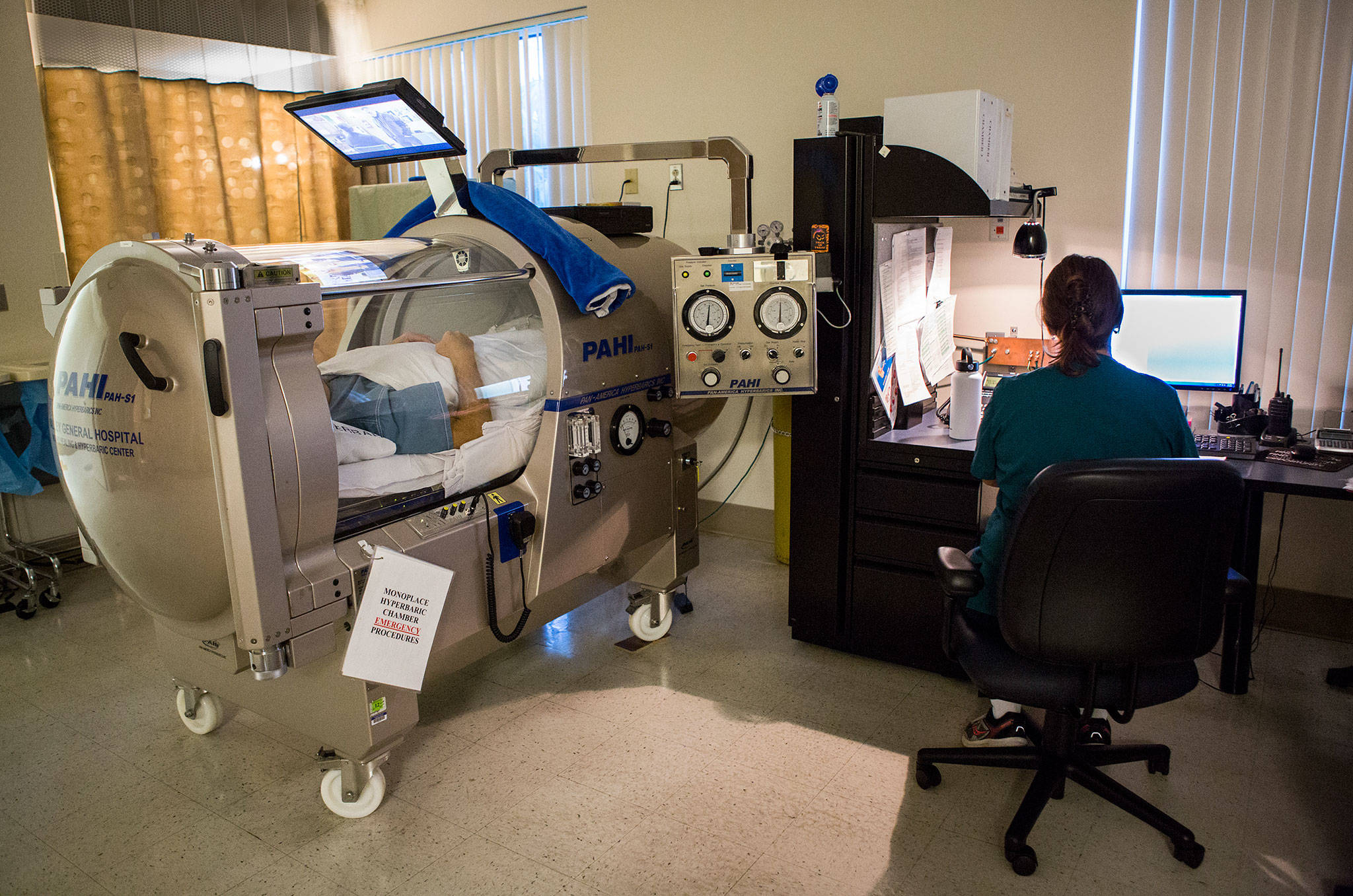 A hyperbaric chamber patient watches television from inside the chamber as a nurse monitors the pressure at EvergreenHealth’s Wound Care and Hyperbarics Center in Monroe. (Olivia Vanni / The Herald)