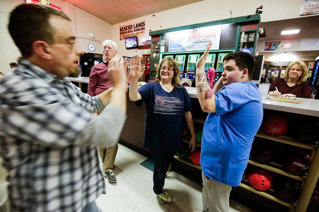 Family members Tony Cea, left, Christi Aquilar, Nick Aquilar (in blue), high five as Vickie Pederson, right, records scores at Glacier Lanes on Jan. 28 in Everett. The family members compete as a team. Tony bowled a 300 recently, one of many in his lifetime. Christie also has bowled a 300. (Andy Bronson / The Herald)
