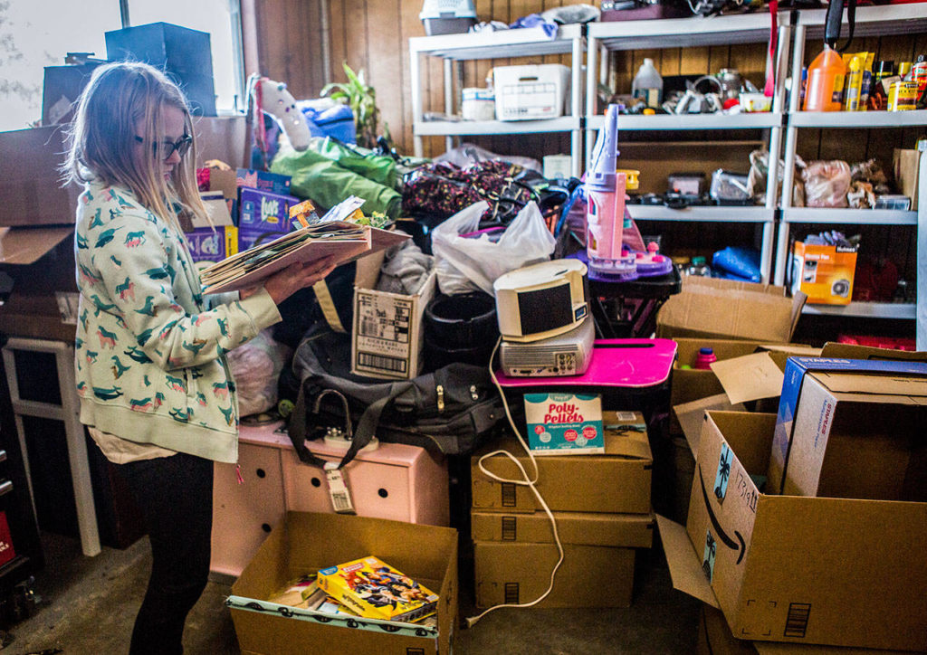Paityn flips through a pop up book Wednesday, Feb. 6 that was donated next to a large pile of donations being stored in their family garage at their home in Snohomish. (Olivia Vanni / The Herald)
