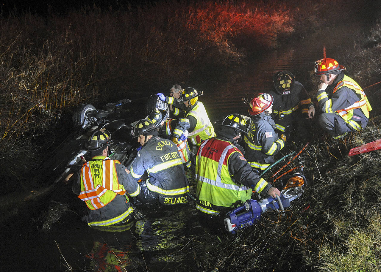 Lake Stevens, Everett and Snohomish firefighters work to free a woman from a vehicle that landed on its top in a water-filled ditch on the north end of Home Acres Road on Ebey Island early Saturday morning. (Doug Ramsay / For the Herald)
