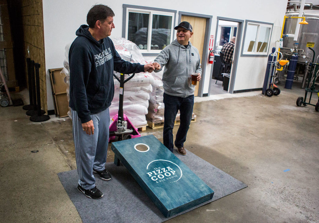 Mark Vogl (left) and Mike Diaz fist-bump after their cornhole game at Bosk Brew Works on Woodinville on Thursday. (Olivia Vanni / The Herald)
