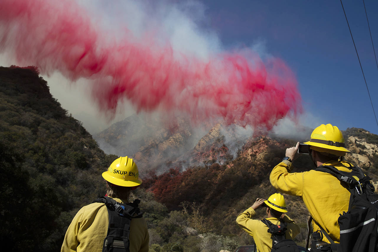 In this Nov. 11, 2018 photo, firefighters take pictures of fire retardant dropped on a burning hillside in Malibu, California. (AP Photo/Jae C. Hong)
