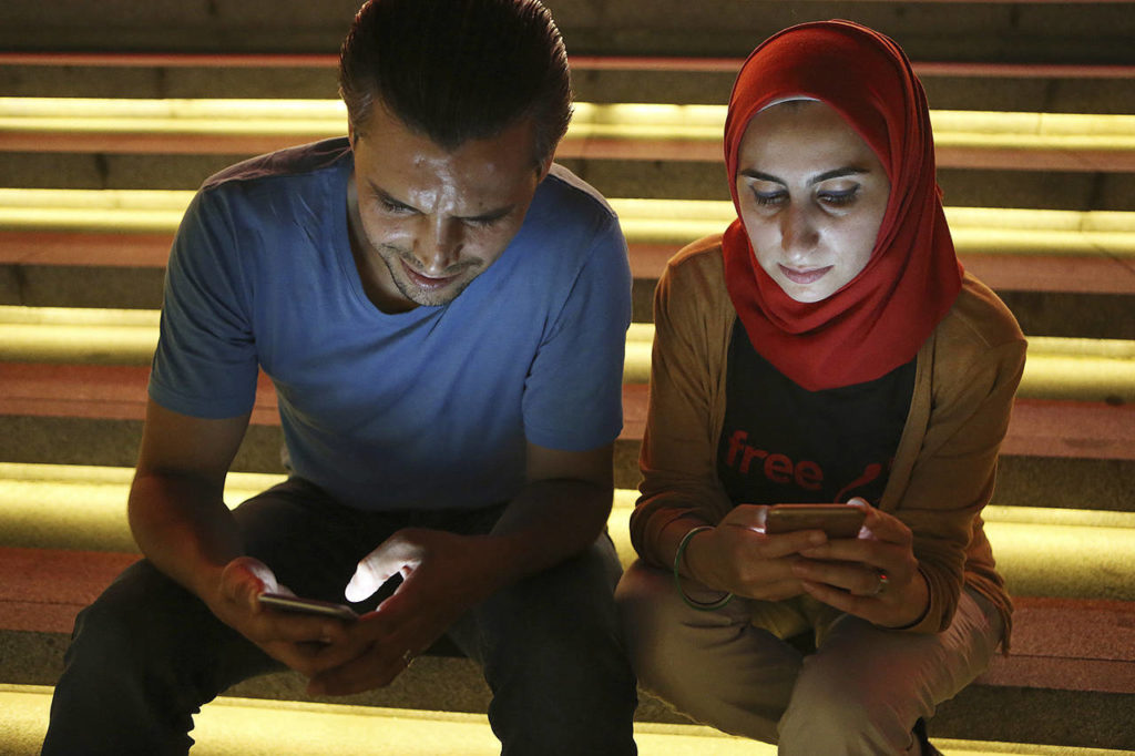 In this 2016 photo, Bahr Abdul Razzak (left) and his wife, Noura Al-Ameer, use their smartphones in Istanbul. The two had been targeted by a mysterious group of undercover operatives, an Associated Press investigation has found. (AP Photo/Petros Karadjias)
