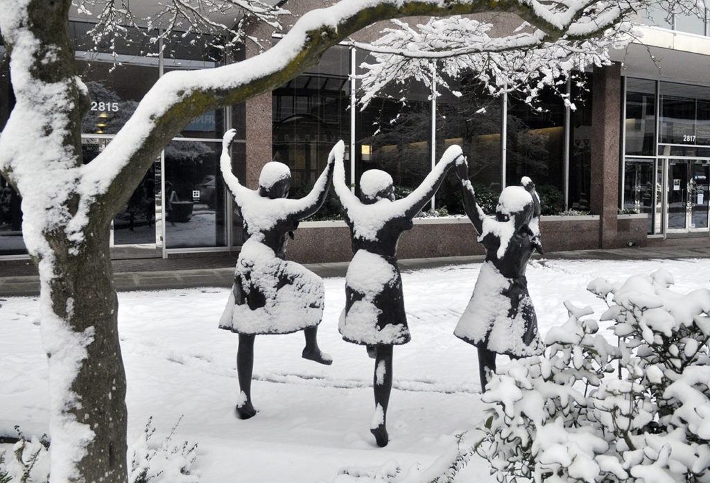 The three girls in the bronze statue “Along Colby” on Colby Avenue in Everett seemed to be dancing for joy in the snow Saturday morning. (Sue Misao / The Herald)
