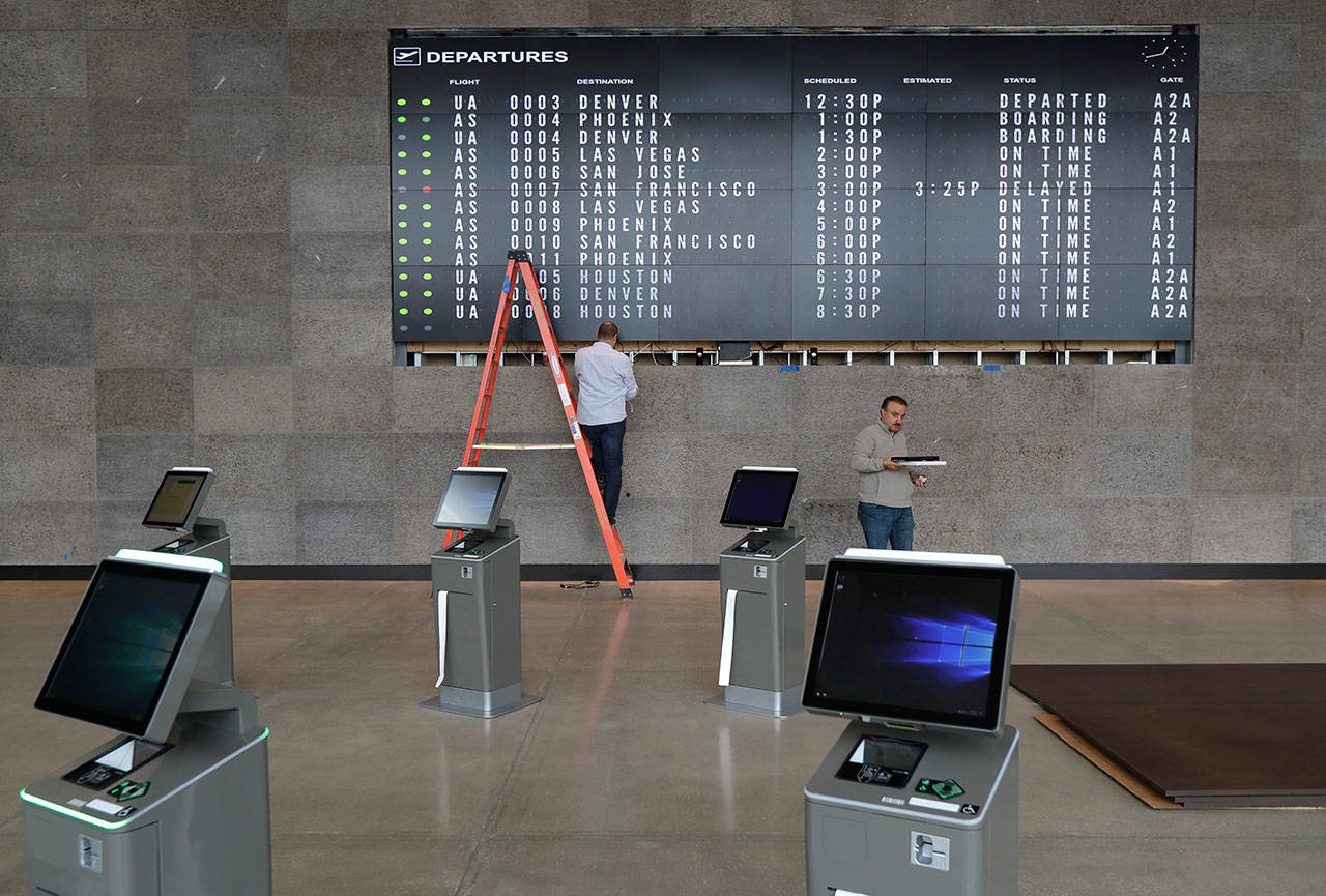 Workers make adjustments on a flight status video display as test destinations are displayed in the new passenger terminal at Paine Field, Jan. 23, 2019, in Everett. Alaska Airlines originally planned to begin service from Paine Field in early February, but last month’s shutdown delayed the start of service until at least early March. (Ted S. Warren / Associated Press)