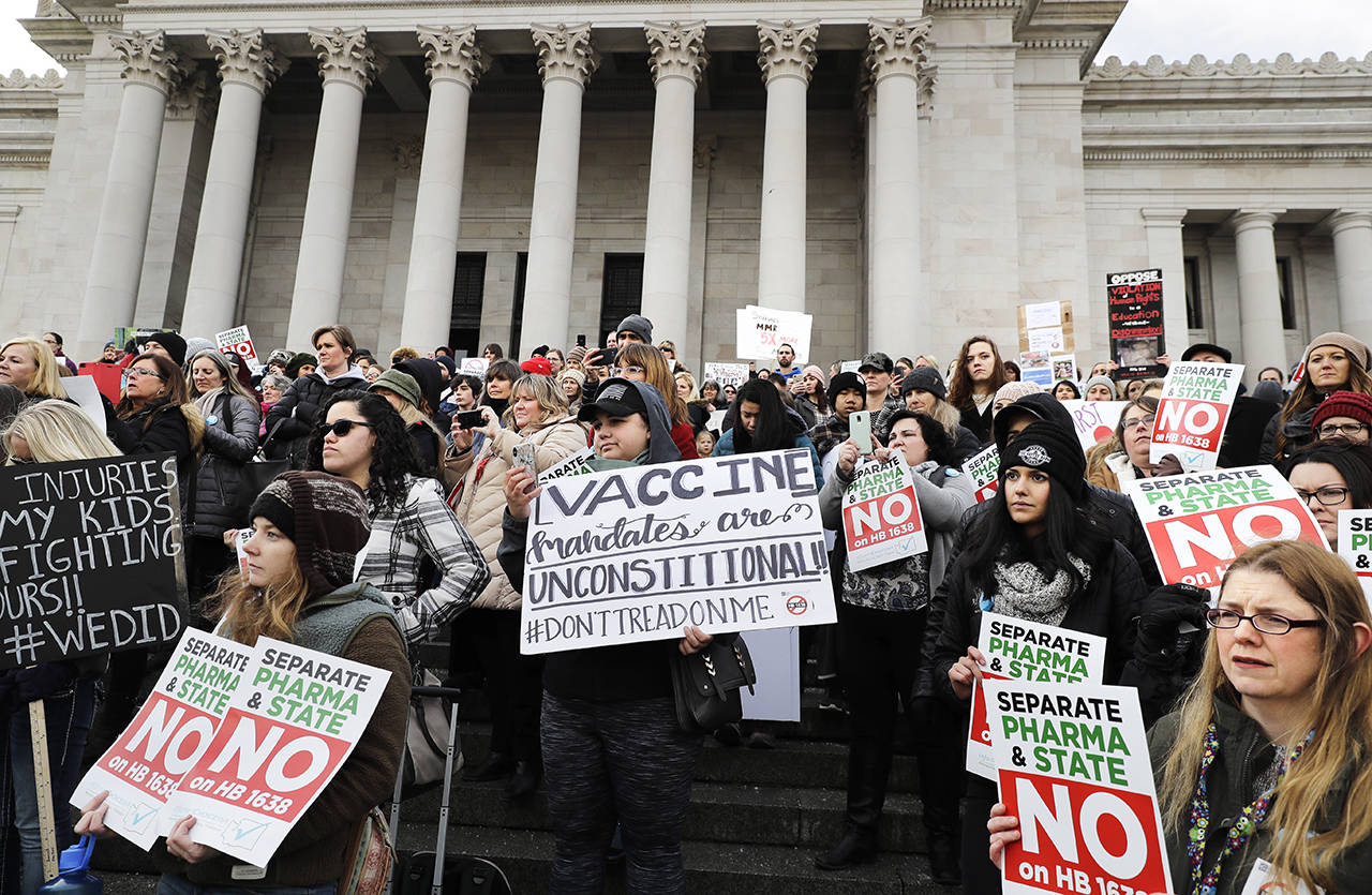 People hold signs at a Feb. 8 rally in Olympia held in opposition to a proposed bill that would remove parents’ ability to claim a philosophical exemption to opt their school-age children out of the combined measles, mumps and rubella vaccine. (AP Photo/Ted S. Warren, file)