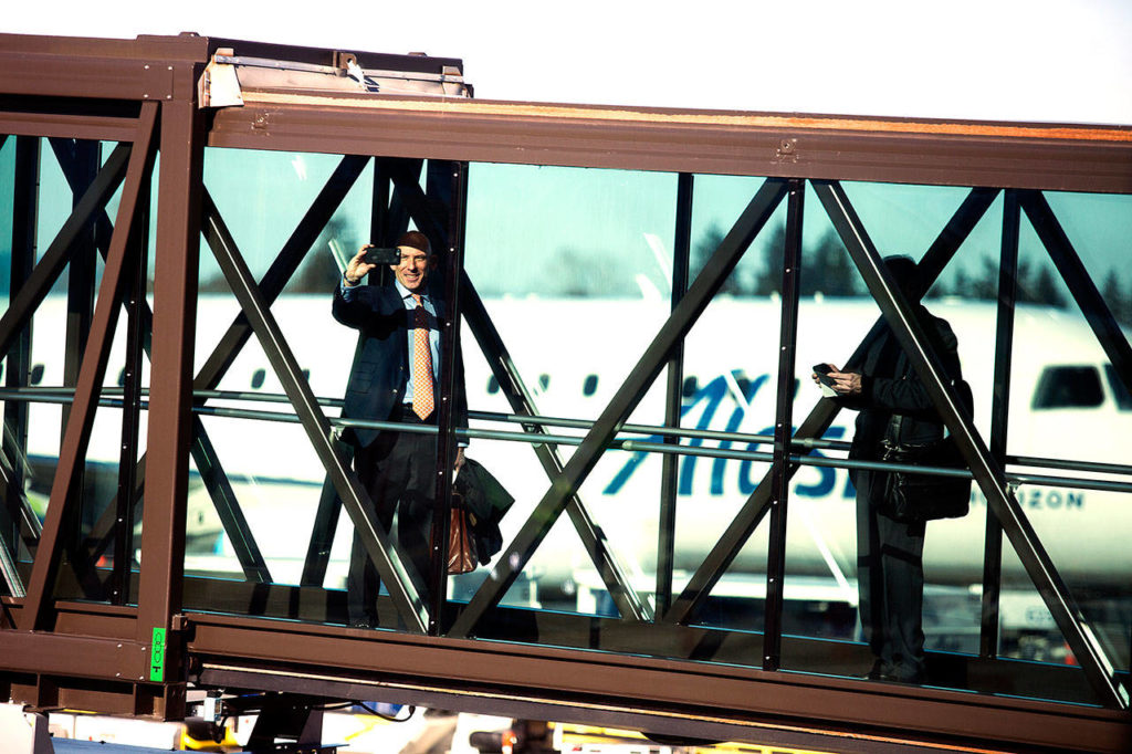 A passenger takes a photo from a glass jet bridge while boarding a plane on opening day of the Paine Field terminal Monday. (Andy Bronson / The Herald)

