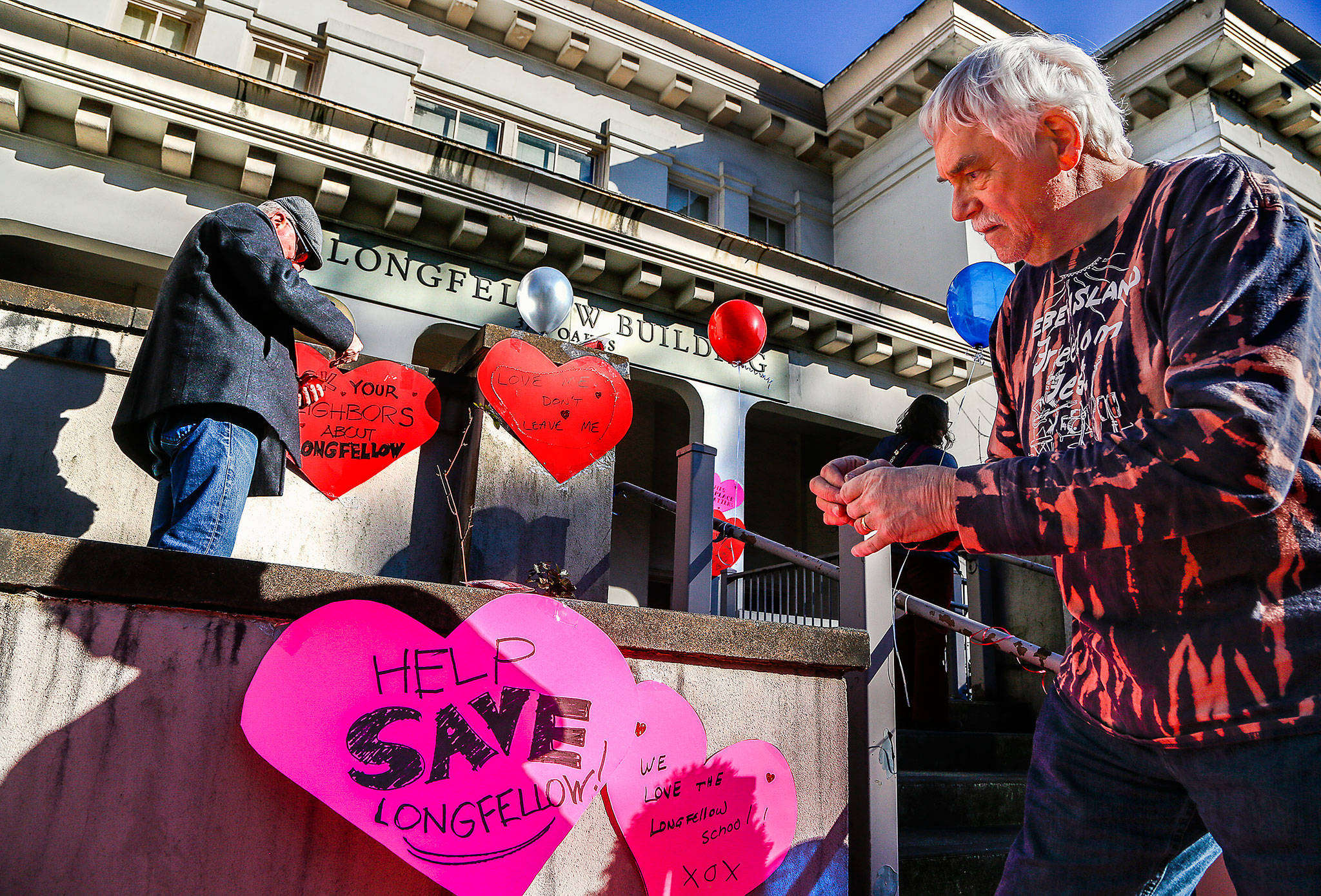photos by Dan Bates / The Herald                                Local preservationists Paul Popelka (right) and Patrick Hall attach paper hearts with messages about the former Longfellow Scholl in Everett o Friday. They are “heart-bombing” the 108-year-old building to raise awareness of plans to demolish it for parking.