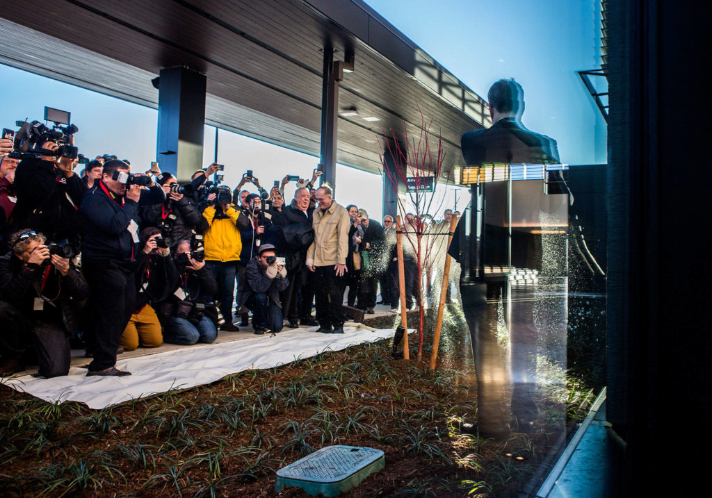 Brett Smith smashes a bottle of champagne against the new building as press take photos during the christening of the Paine Field Airport on March 4 in Everett. (Olivia Vanni / The Herald)
