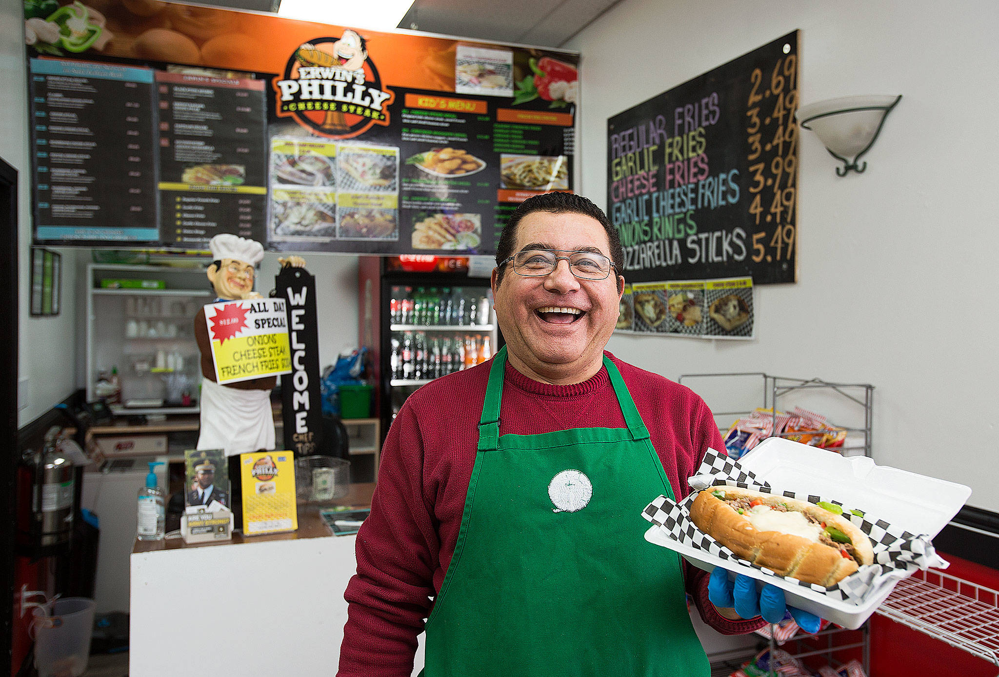 Erwin Sanchez, owner of Erwin’s Philly Cheese Steak, holds up one of the selections from the menu at his Everett restaurant. (Andy Bronson / The Herald)