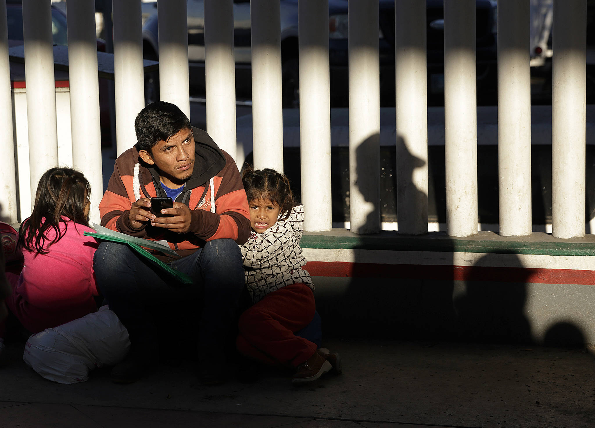In this Jan. 25 photo, a migrant who did not give his name looks on with his children as they wait to hear if their number is called to apply for asylum in the United States, at the border in Tijuana, Mexico. (AP Photo/Gregory Bull, File)