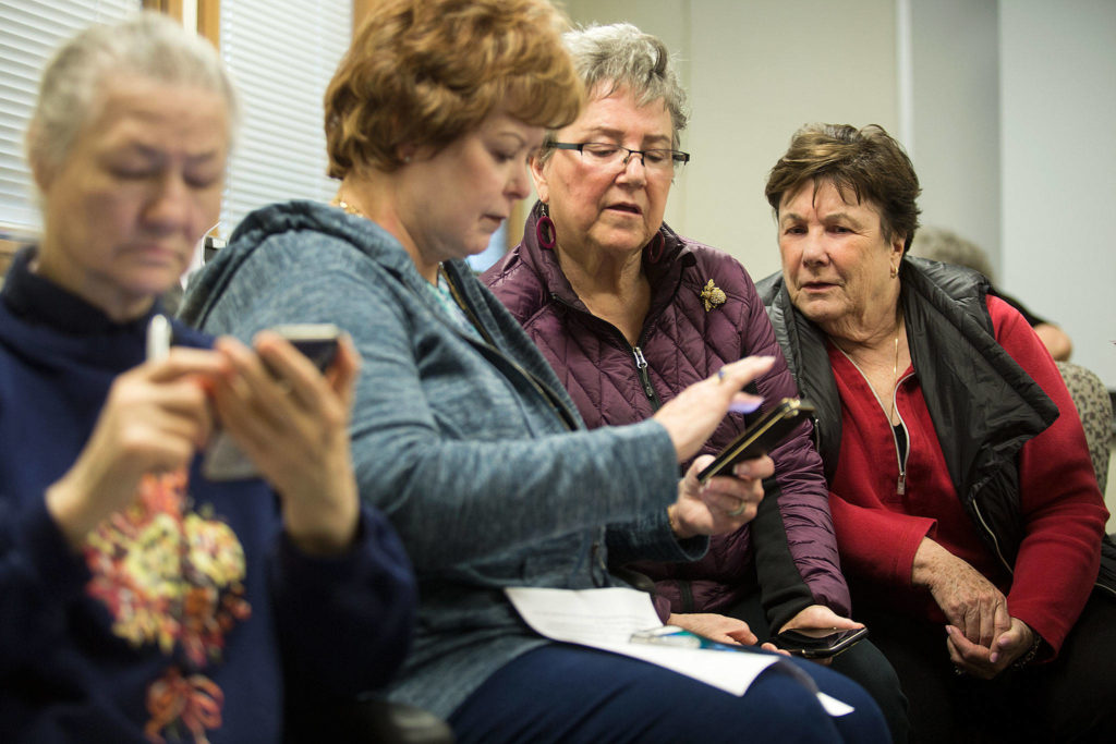 Gretchen Mork (right) watches as Connie Castruita (center) swipes to close a bunch of programs on her phone during a smartphone class at the Carl Gipson Senior Center on Feb. 1, 2018, in Everett. (Andy Bronson / Herald file)
