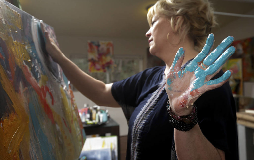 Blue paint coats one of Cort’s hands as she paints in her Snohomish studio. (Andy Bronson / The Herald)
