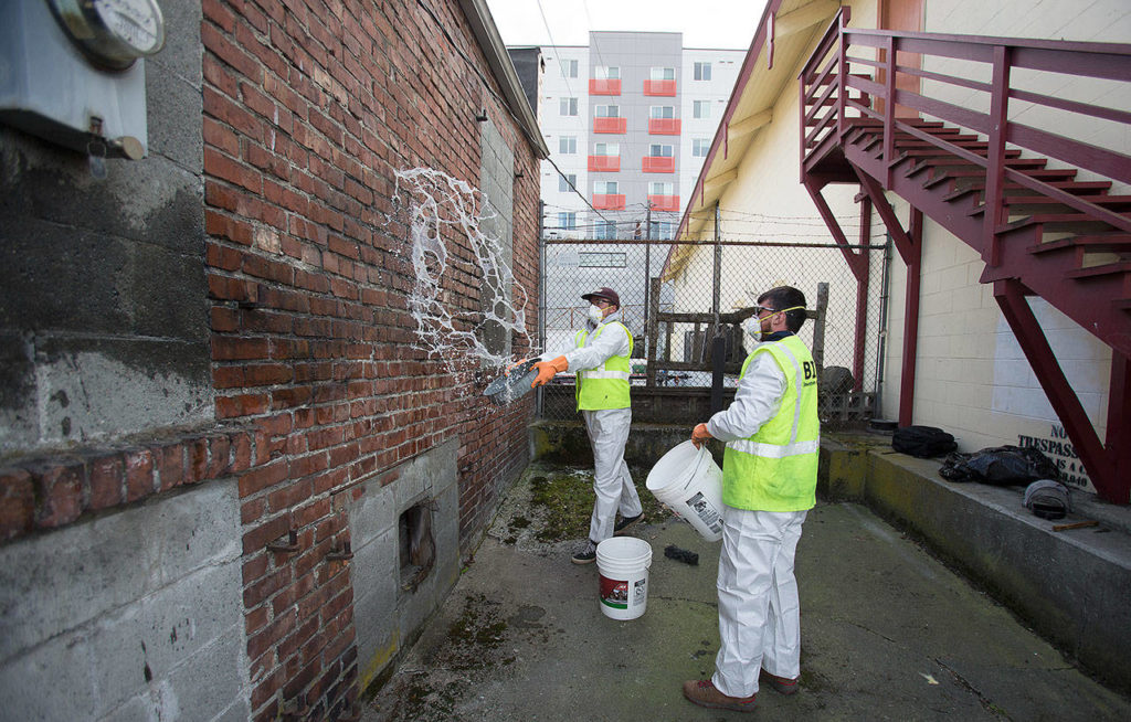 Business Improvement Association’s Trevor Dodge splashes water on a wall just cleaned of graffiti at Charlie’s Combat Club in downtown on Thursday, March 21, 2019 in Everett, Wash. Cody MacDouglal waits to use a second bucket of water to finish the cleaning. (Andy Bronson / The Herald)
