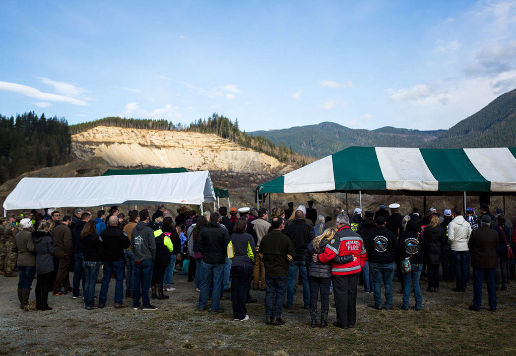 A couple embraces as the sun breaks through to illuminate part of the slide site during the remembrance ceremony on Friday near Oso. (Olivia Vanni / The Herald) 
