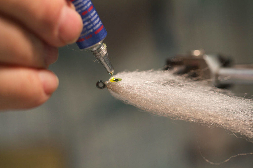 A tier applies glue activated by ultraviolet light to lock in a plastic eye on a small baitfish pattern. (Mike Benbow)
