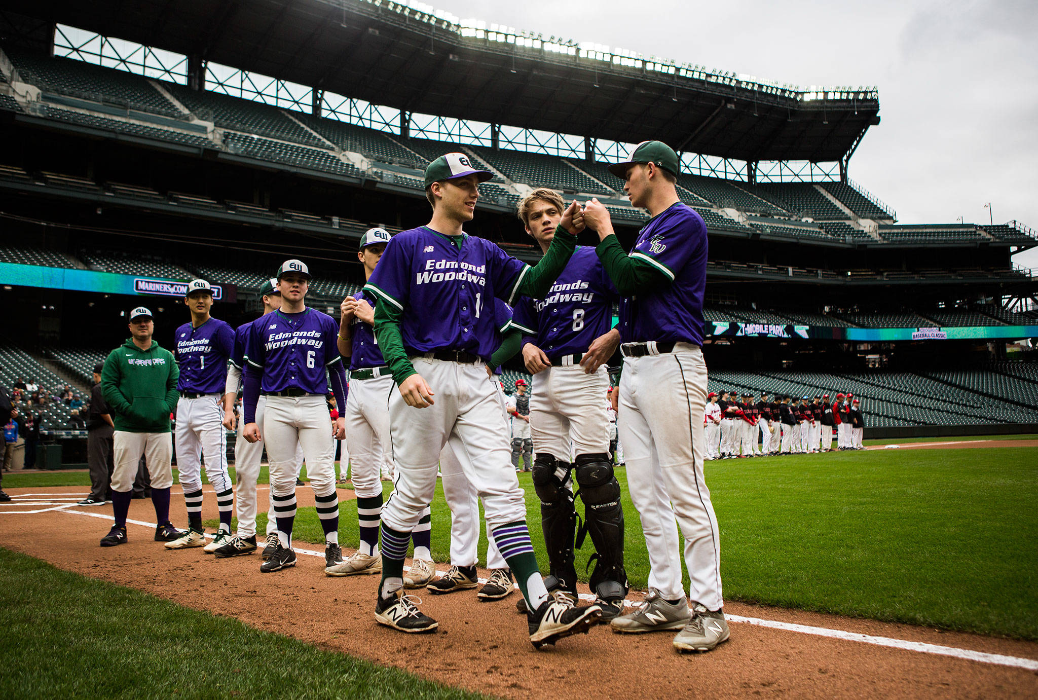 Edmonds-Woodway’s Karsen Tjarneberg walks down the first-base line and fist-bumps his teammates prior to Sunday’s game at T-Mobile Park, formerly known as Safeco Field. The Warriors faced Mount Si at the Seattle Mariners’ ballpark as part of the annual High School Baseball Classic. (Olivia Vanni / The Herald)