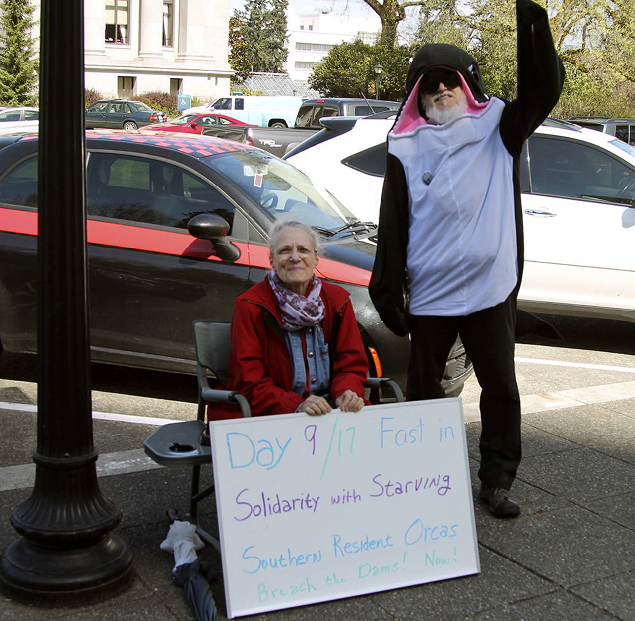 Lanni Johnson sits in front of the Capitol building steps where she has been on a hunger strike to save the Southern Resident orcas. She is joined by supporter Phil Myers, who is wearing an orca onesie. (Emma Epperly / WNPA Olympia News Bureau)