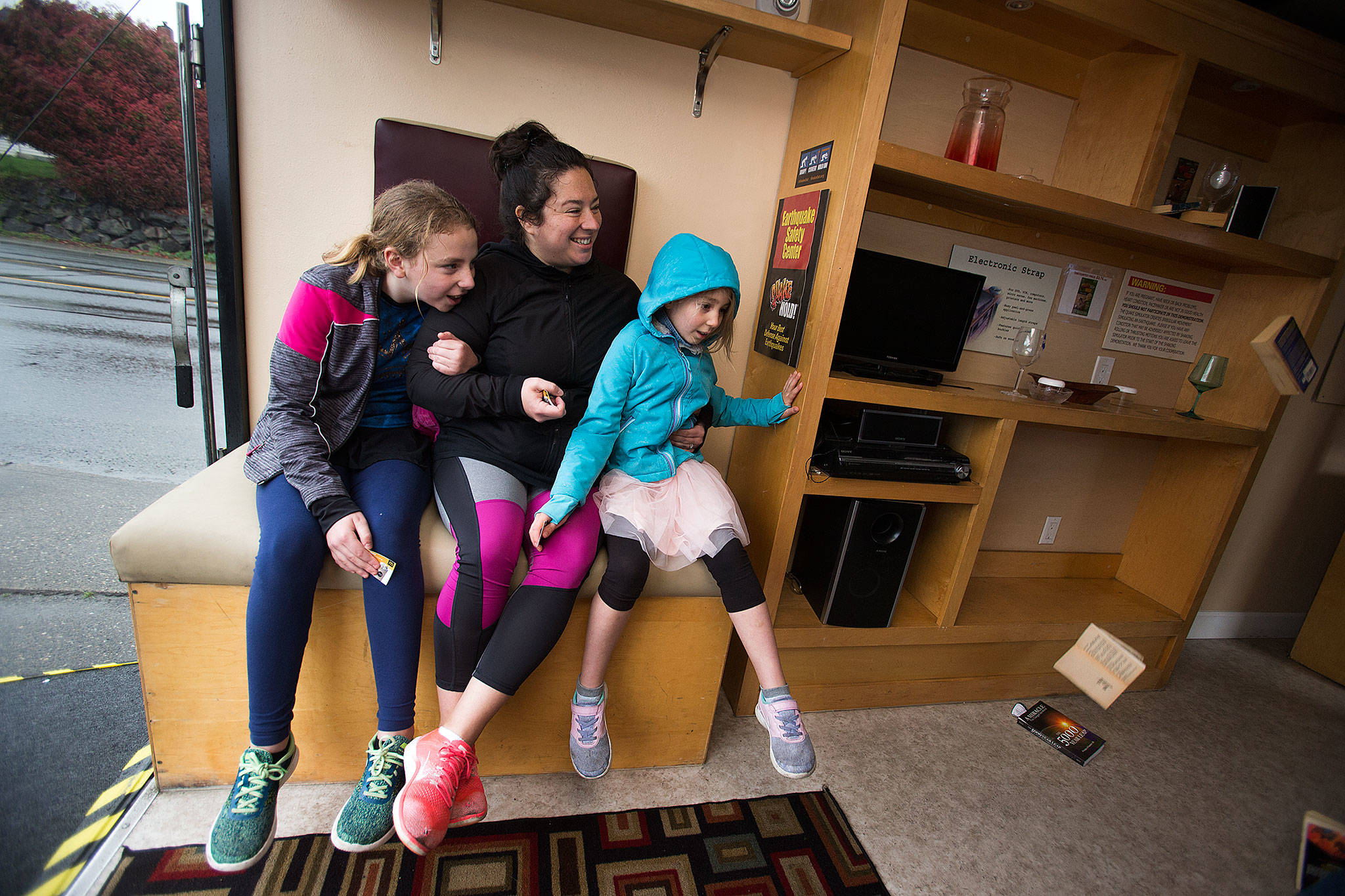 Betty Davis, left, holds on to her mother Leia, who holds onto daughter Alana,7, as they watch books fall from shelves inside The Big Shaker as it shakes like a magnitude 8 earthquake on April 19 in Everett. The Big Shaker is an earthquake simulator in a 24-foot trailer that replicates a typical living room of sofas and shelves with books and plastic dishes that fall during the demonstration. (Andy Bronson / The Herald)