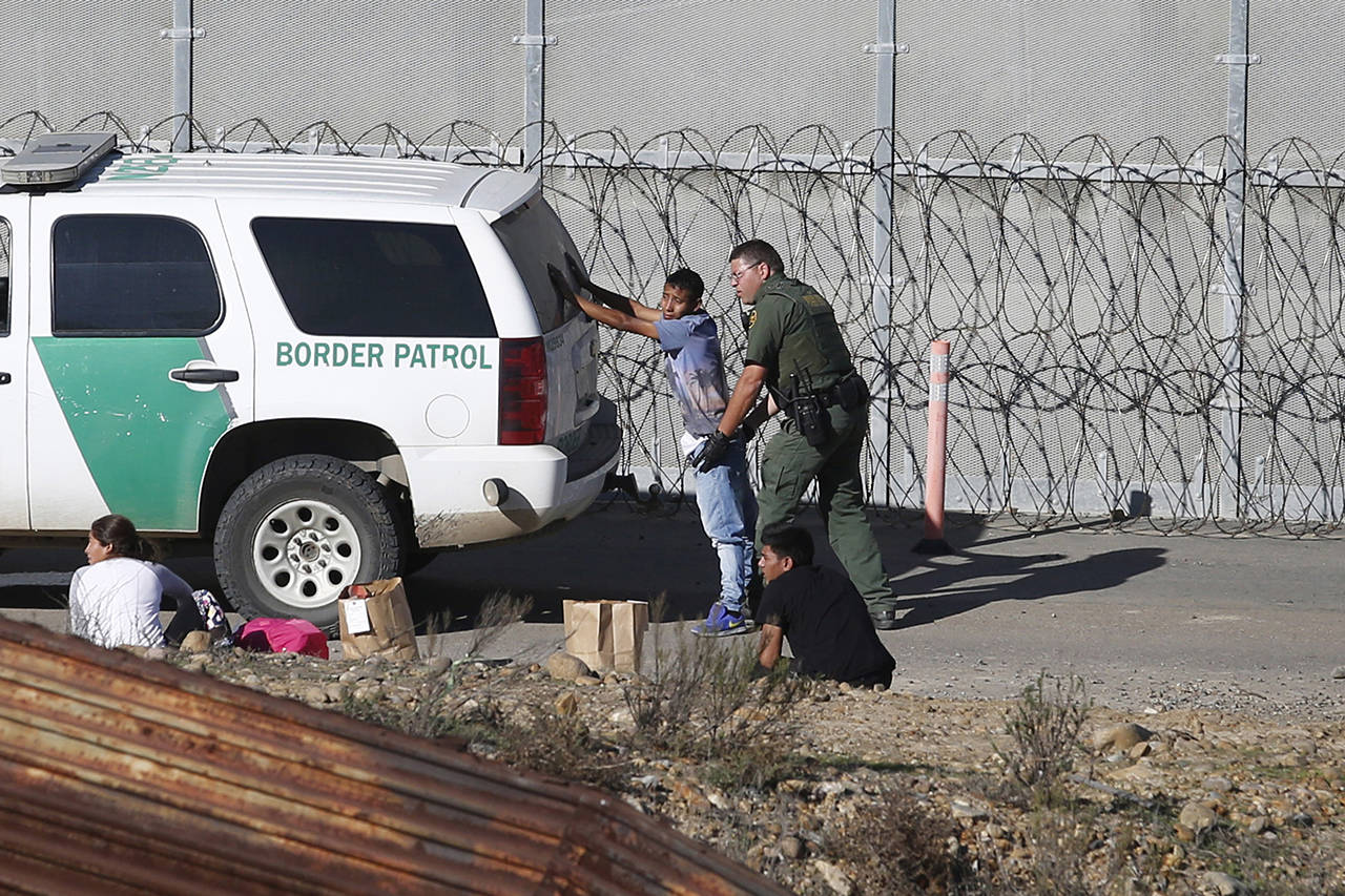 In this Dec. 2018 photo, Honduran asylum seekers are taken into custody by U.S. Border Patrol agents after the group crossed the U.S. border wall into San Diego, California, seen from Tijuana, Mexico. Detained asylum seekers who have shown they have a credible fear of returning to their country will no longer be able to ask a judge to grant them bond. (AP Photo/Moises Castillo, File)