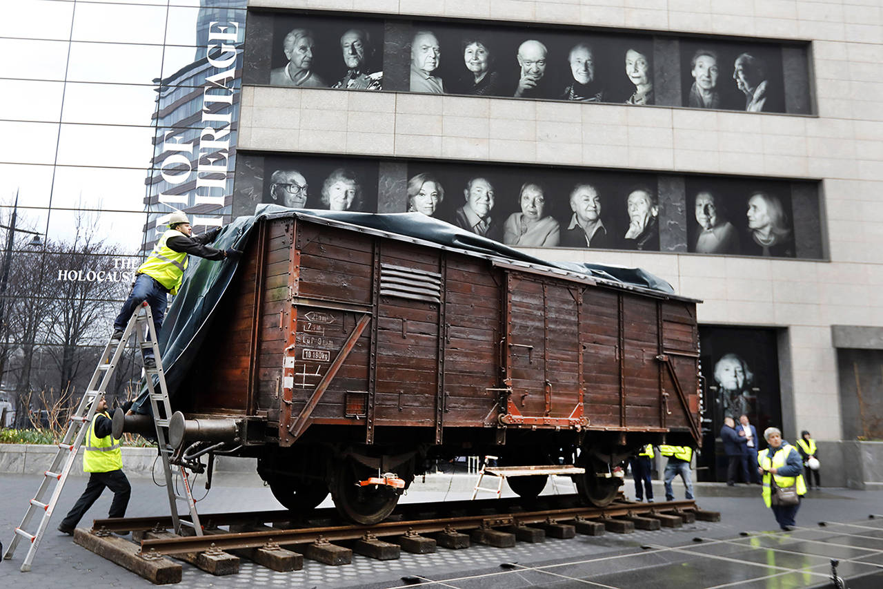 Portraits of Holocaust survivors are displayed at the Museum of Jewish Heritage as a vintage German train car, like those used to transport people to Auschwitz and other death camps, is uncovered on tracks outside the museum, in New York on March 31. Schools in Washington will be ‘strongly encouraged’ to teach about the Holocaust under a bill signed into law by Gov. Inslee. (AP Photo/Richard Drew)