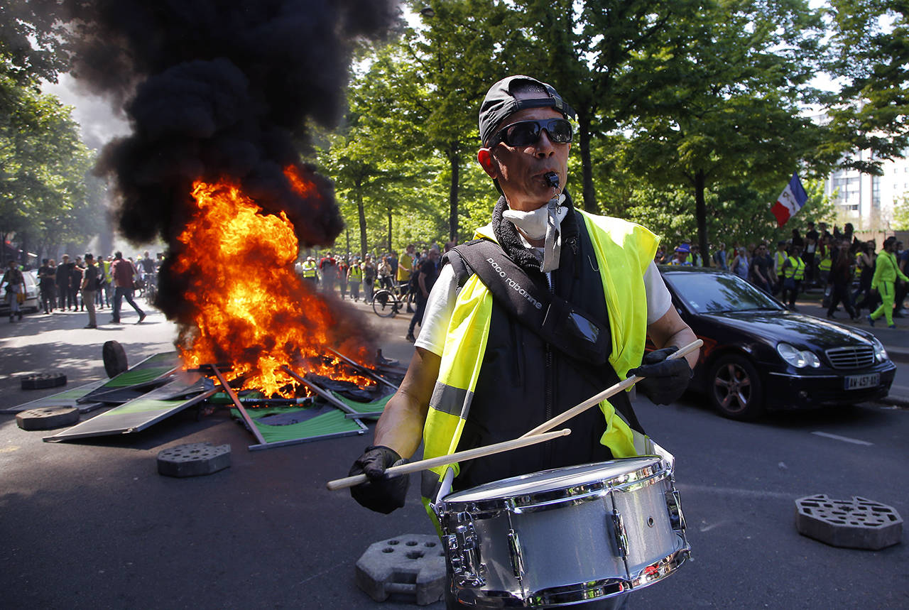 A man bangs a drum in front of a fire on the street during a yellow vest demonstration in Paris on Saturday. (AP Photo/Michel Euler)