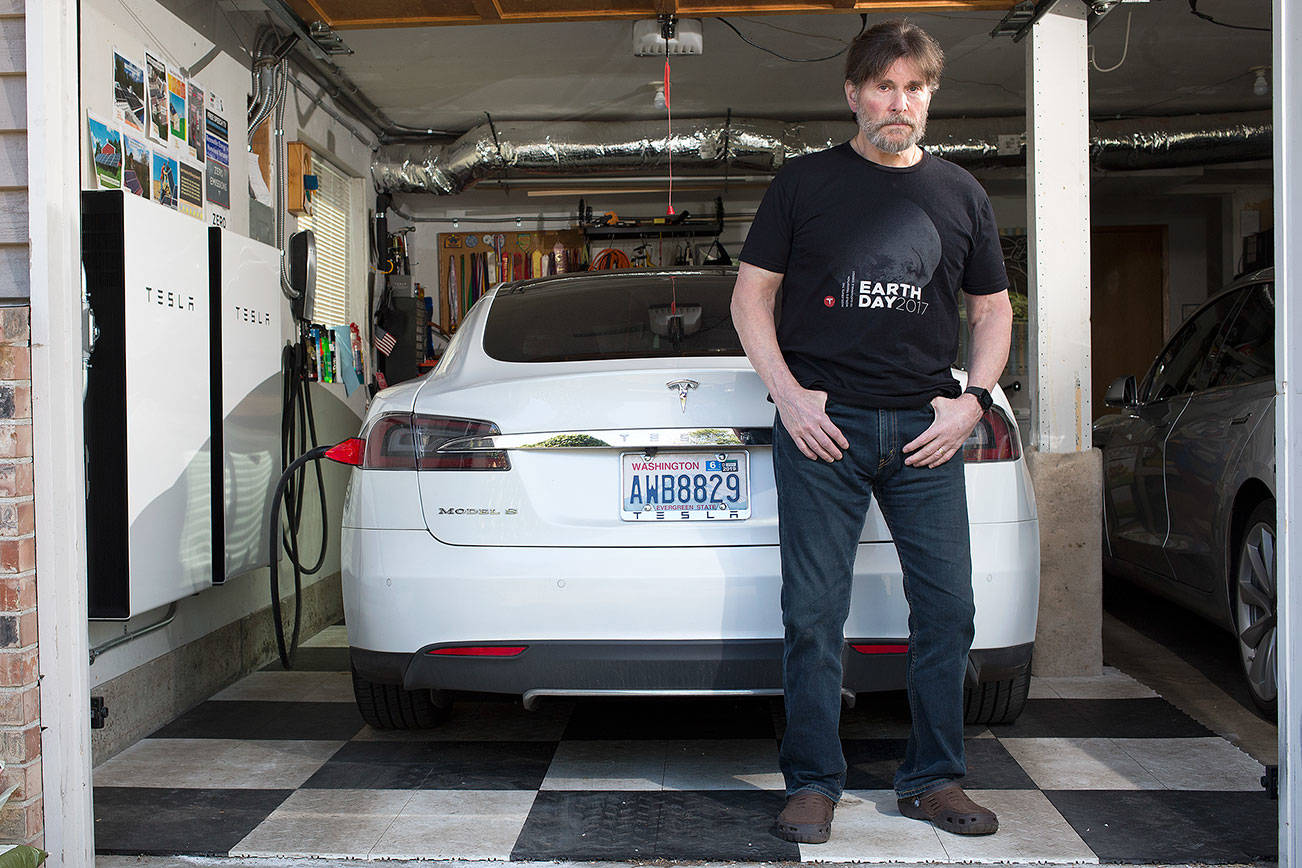 David Kendall stands in front of one of two Tesla cars and two Tesla Powerwall batteries hanging in his garage on Wednesday, April 24, 2019 in Edmonds, Wash. (Andy Bronson / The Herald)