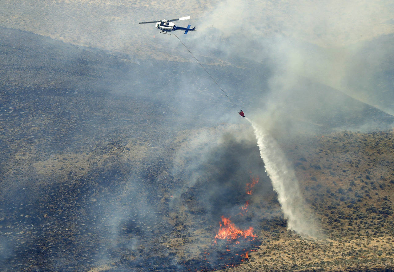 In this June 2018 photo, a helicopter uses a bucket to drop water on the Milepost 22 wildfire near Vantage, Washington. (AP Photo/Ted S. Warren, File)
