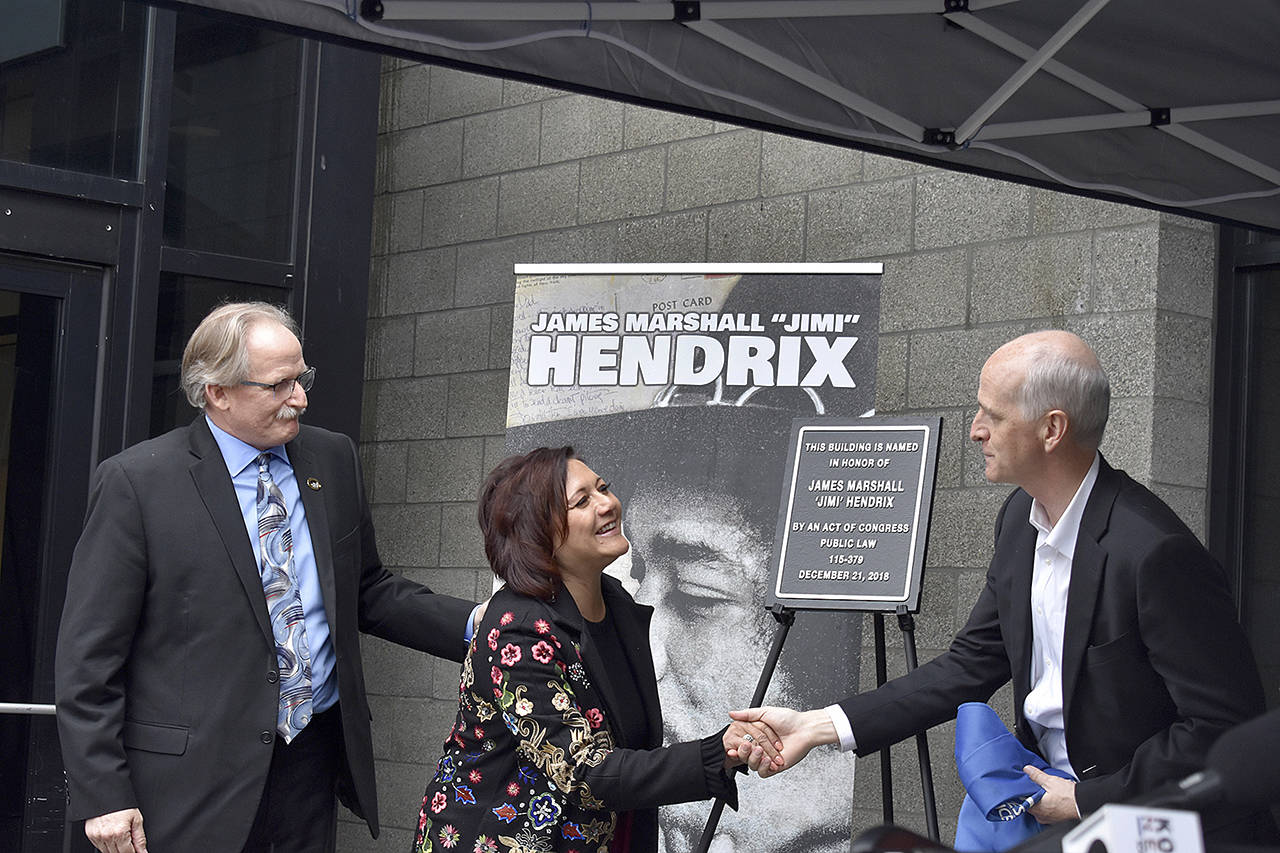 USPS district manager Darrell Stoke, Janie Hendrix and Congressman Adam Smith unveil the plaque honorarily naming the Renton Highlands Post Office as the “James Marshall ‘Jimi’ Hendrix Post Office” on April 19 in Renton. (Haley Ausbun / Renton Reporter)